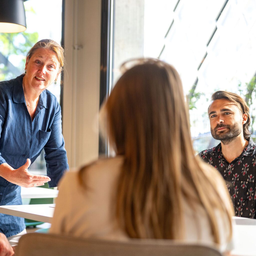Medewerkers in gesprek tijdens een teamoverleg over samenwerking, feedback en het bespreekbaar maken van gedrag binnen een gezonde aanspreekcultuur.
