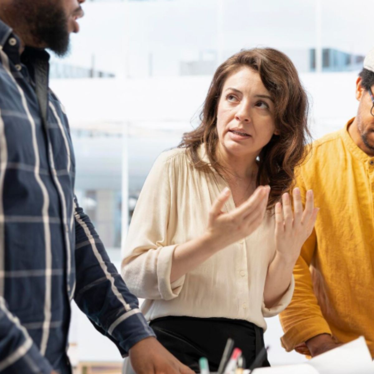 Collega’s bespreken een lastige situatie op de werkvloer; een vrouw reageert zichtbaar op weerstand in het gesprek, terwijl anderen meeluisteren.